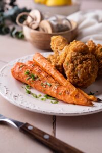 Grilled carrots garnished with parsley and served with fried chicken on a white plate.