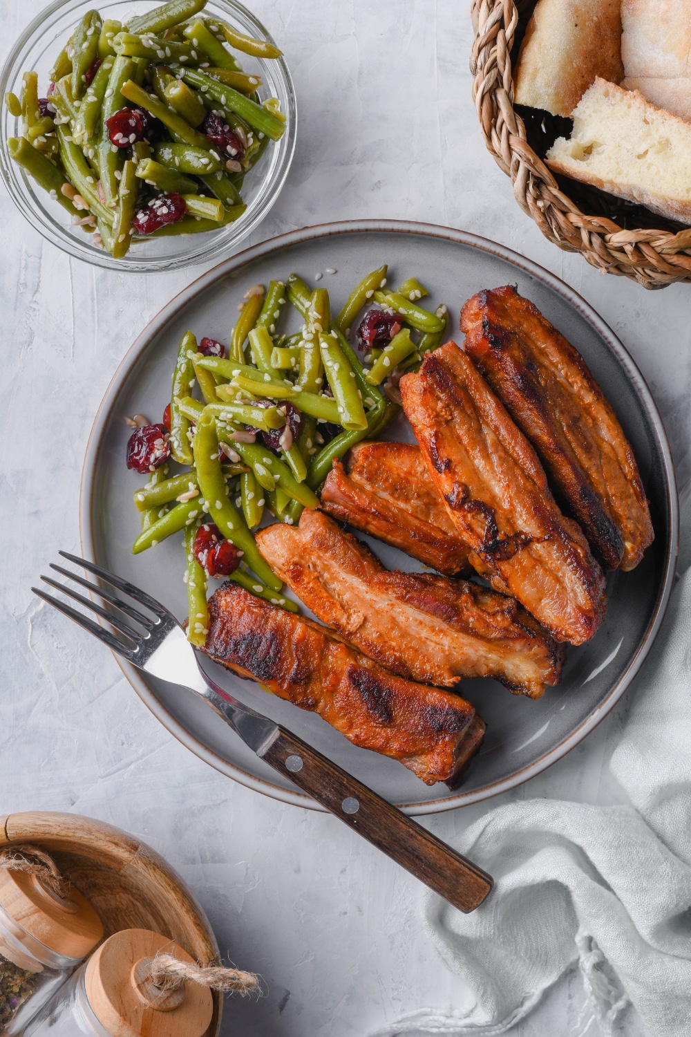 Top view of roasted pork belly strips with green bean salad on a gray plate with a fork.