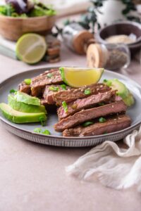 Sirloin tip steak on a plate, sliced and served with avocado slices and lime wedges.