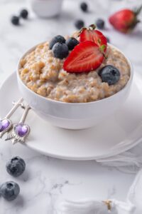 Steel cut oatmeal topped with blueberries and sliced strawberries, served in a white bowl set over a plate.