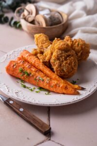 Grilled carrots served with fried chicken and garnished with parsley.