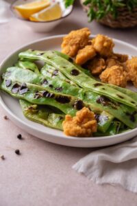 Grilled green beans served with chicken nuggets on a white plate.