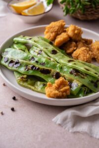 Grilled green beans served with chicken nuggets on a white plate.