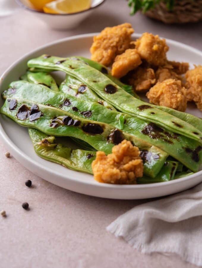 Grilled green beans served with chicken nuggets on a white plate.