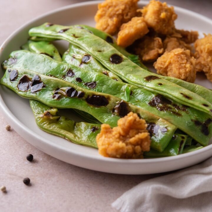 Grilled green beans served with chicken nuggets on a white plate.