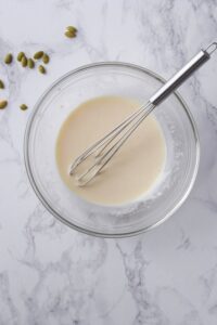 Mixed creamy salad dressing in a glass bowl with a whisk.