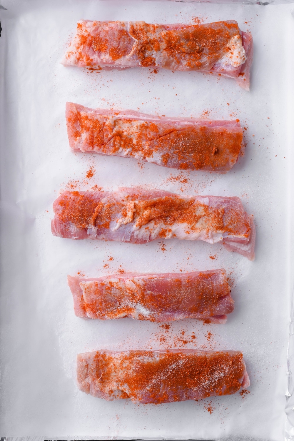 Seasoned raw pork belly strips on a parchment paper.