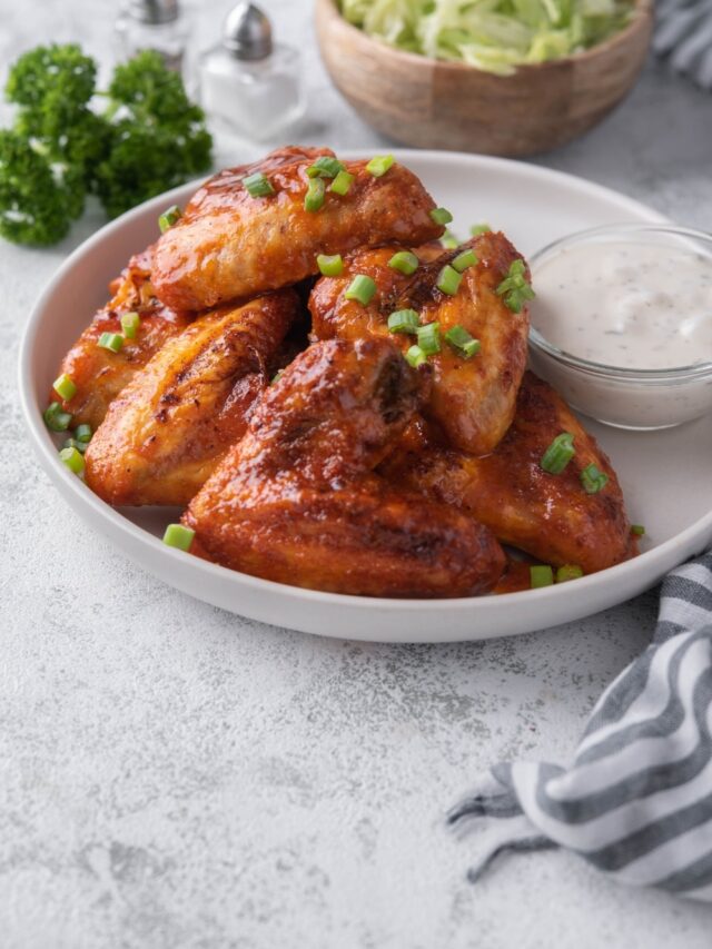 Baked chicken wings on a plate garnished with chopped green onions and served with ranch.