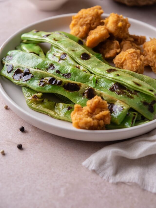 Grilled green beans served with chicken nuggets on a white plate.