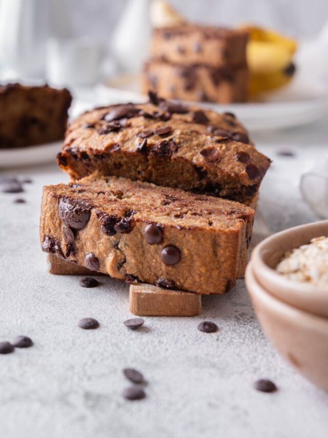 Sliced chocolate chip oatmeal banana bread on a wood cutting board. Behind are more plate of banana bread slices.