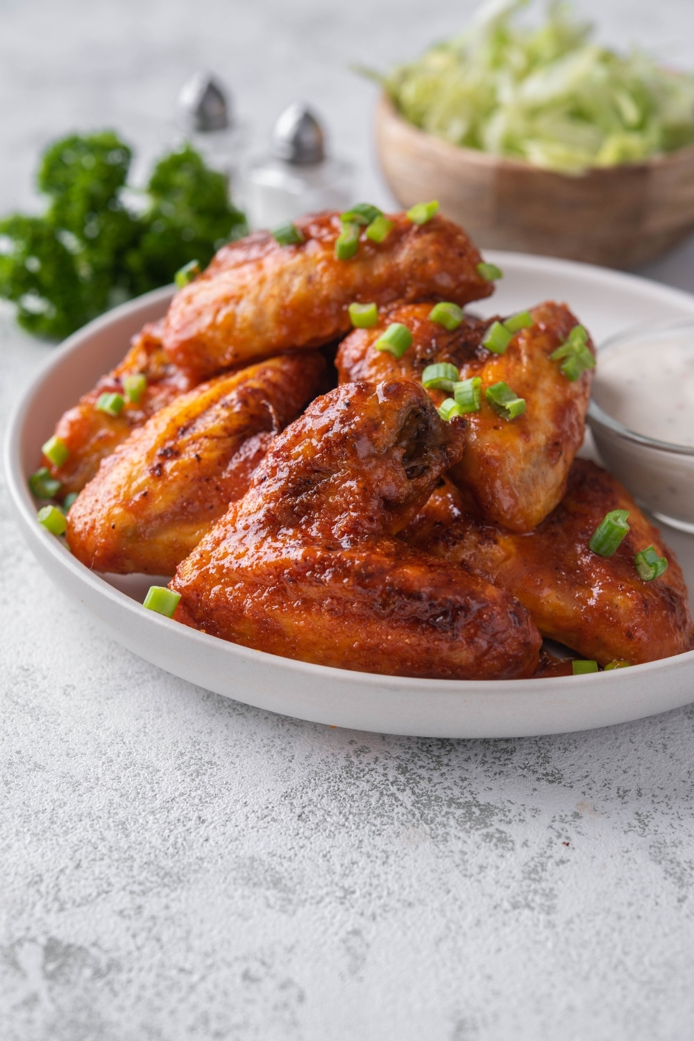 Baked chicken wings topped with chopped green onions and served with a small bowl of ranch.