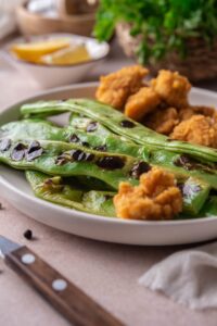 Grilled green beans and fried chicken nuggets on a white plate.