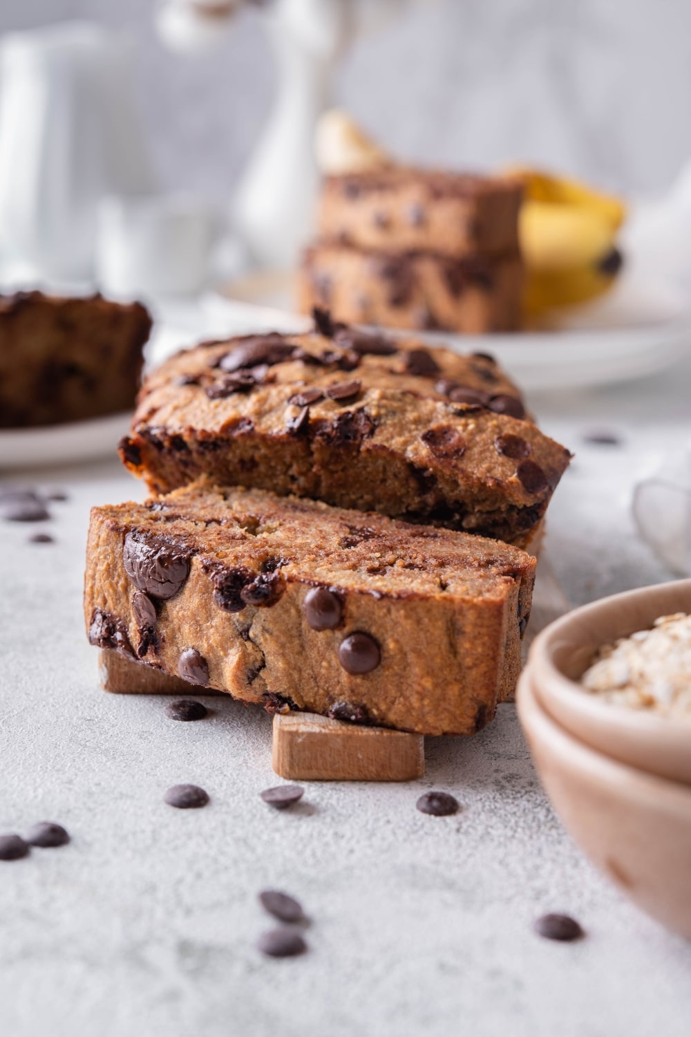 Sliced chocolate chip oatmeal banana bread on a wood cutting board. Behind are more plate of banana bread slices.