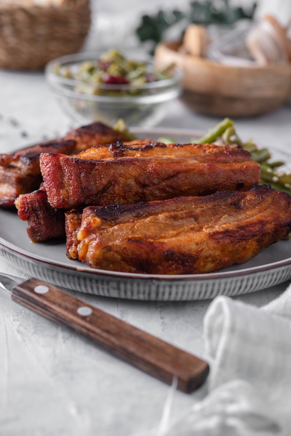 Roasted pork belly on a plate served with green bean salad. In the back is a small bowl of green bean salad.