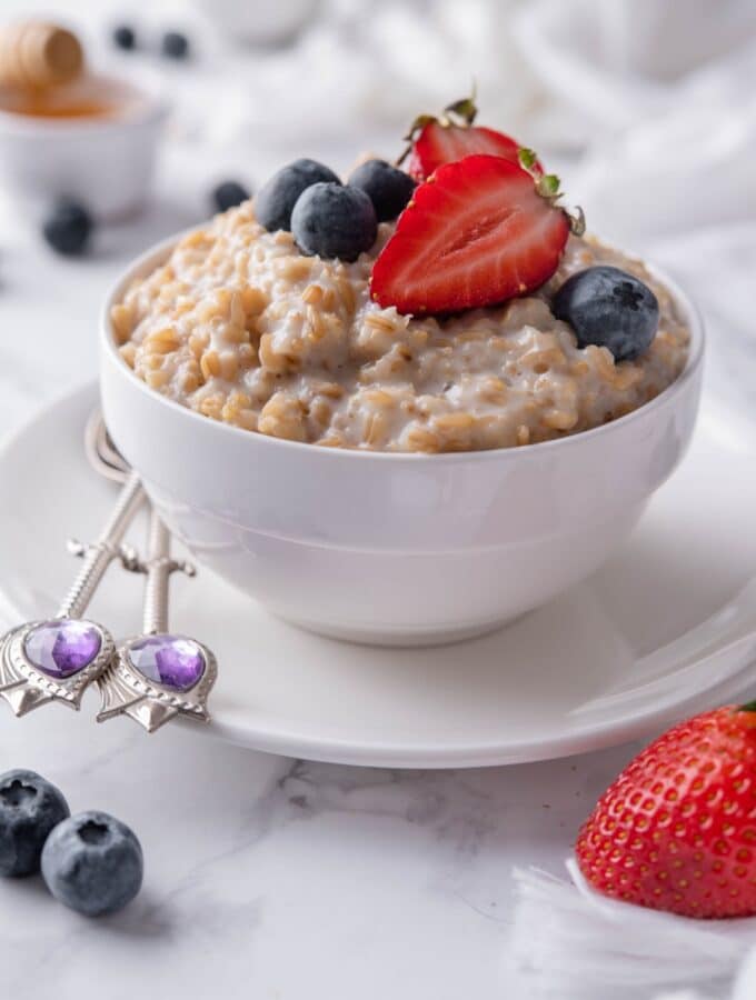 Creamy steel cut oats topped with blueberries and sliced strawberries in a white bowl set over a plate.