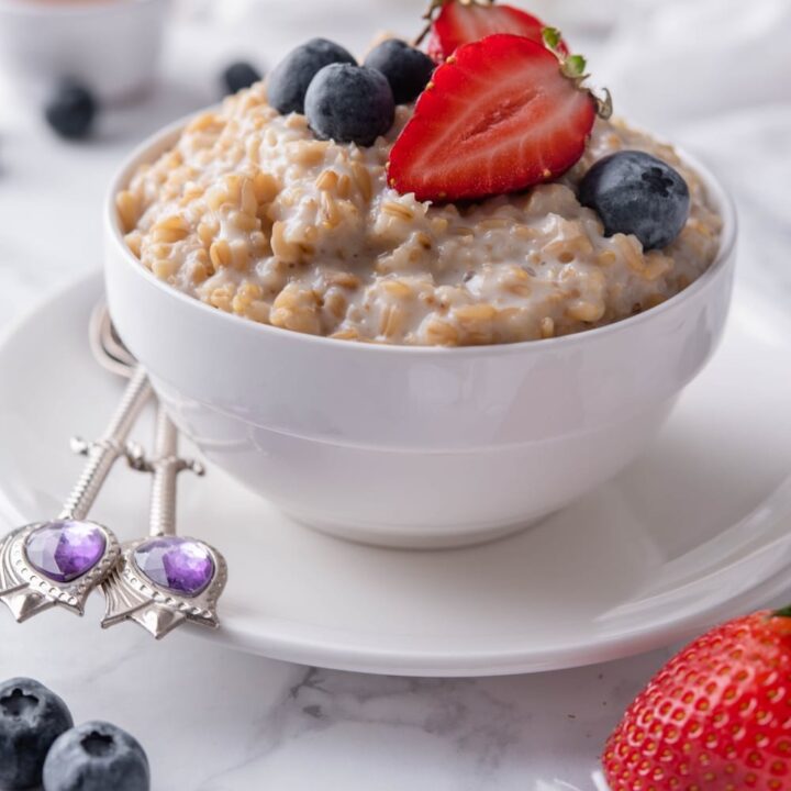 Creamy steel cut oats topped with blueberries and sliced strawberries in a white bowl set over a plate.