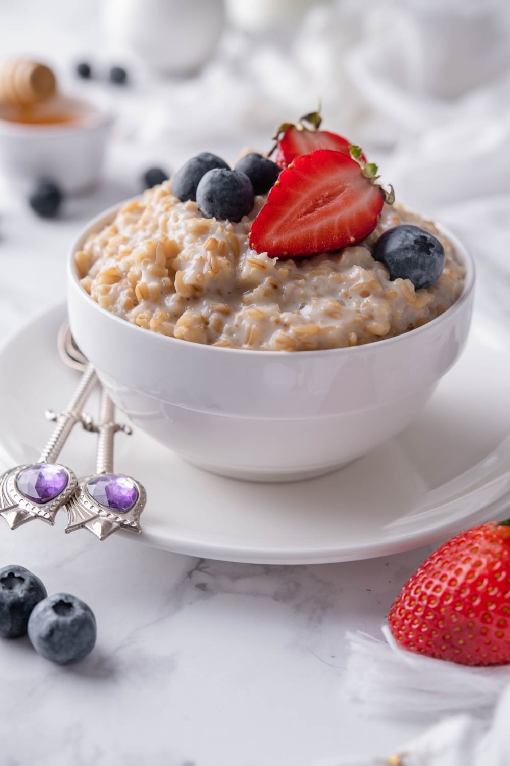 Creamy steel cut oats topped with blueberries and sliced strawberries in a white bowl set over a plate.