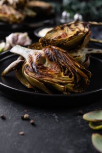 A closer look at grilled artichoke halves served on a black plate.