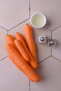 Raw carrots, a small bowl of oil, and salt and pepper shakers.