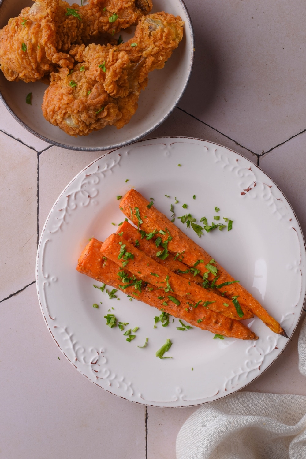 Grilled carrots garnished with parsley on a plate, next to a plate of fried chicken.