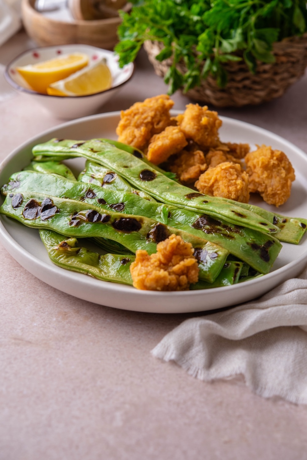 Chicken nuggets and grilled green beans on a plate, served with a small bowl of lemon wedges.