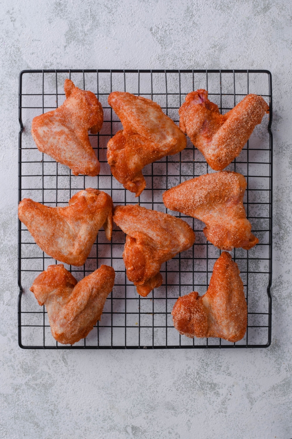 Eight seasoned chicken wings on a baking rack.