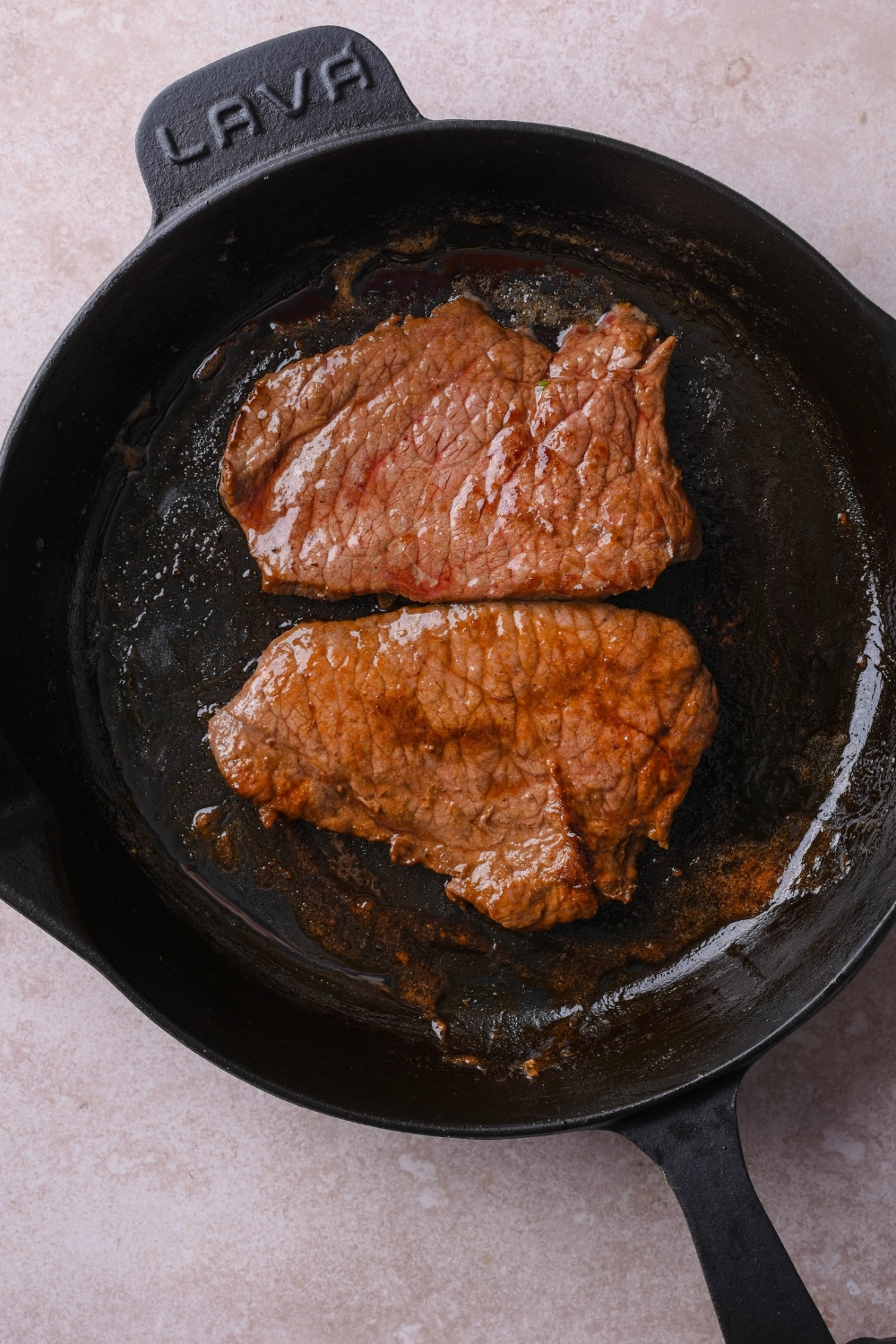 Two pieces of sirloin tip steak on a cast iron pan.