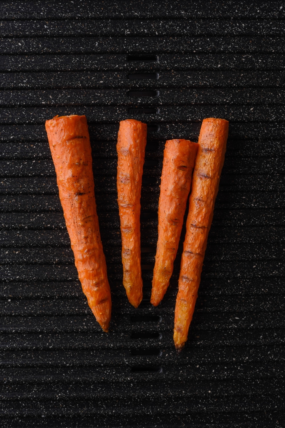 Four grilled carrots on an electric grill.