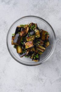 Roasted eggplant tossed with minced garlic and chopped parsley in a glass bowl.
