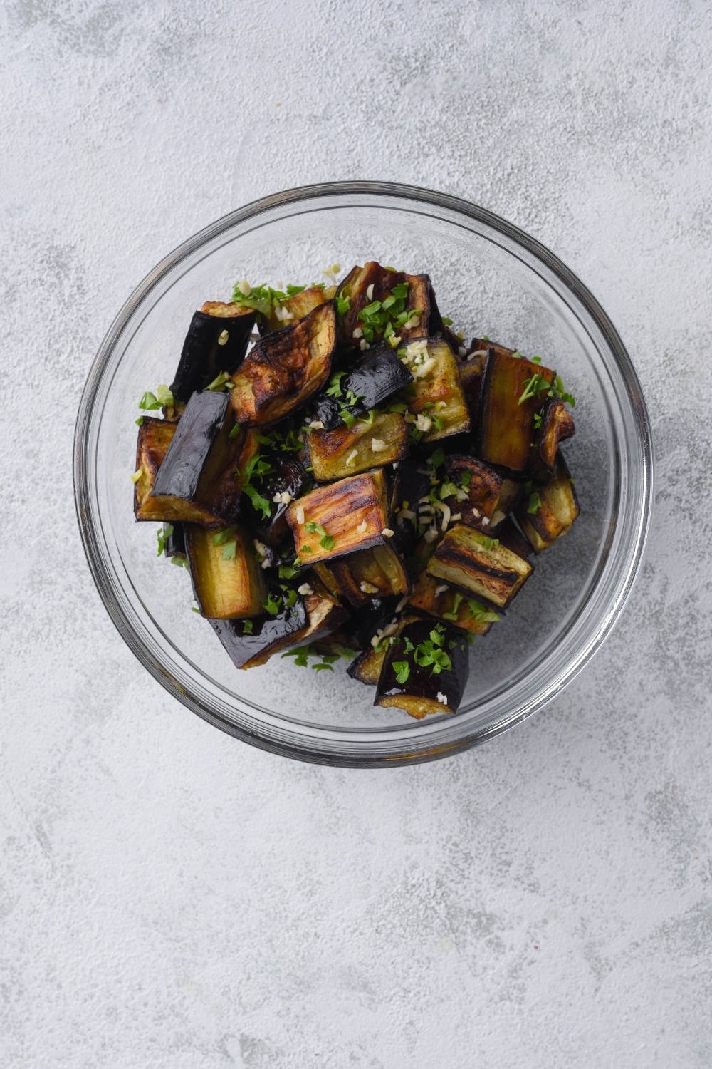 Roasted eggplant tossed with minced garlic and chopped parsley in a glass bowl.
