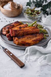 Roasted pork belly strips served with green bean salad. In the back is a small bowl of green bean salad.