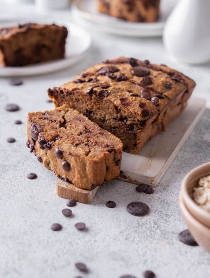 Sliced oatmeal chocolate chip banana bread on a wooden serving board, in front of two more plate of banana bread slices.