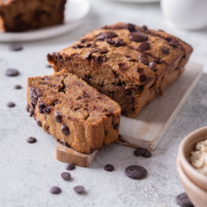 Sliced oatmeal chocolate chip banana bread on a wooden serving board, in front of two more plate of banana bread slices.