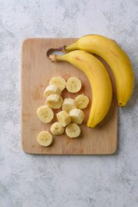 Sliced bananas and whole bananas on a wooden cutting board.
