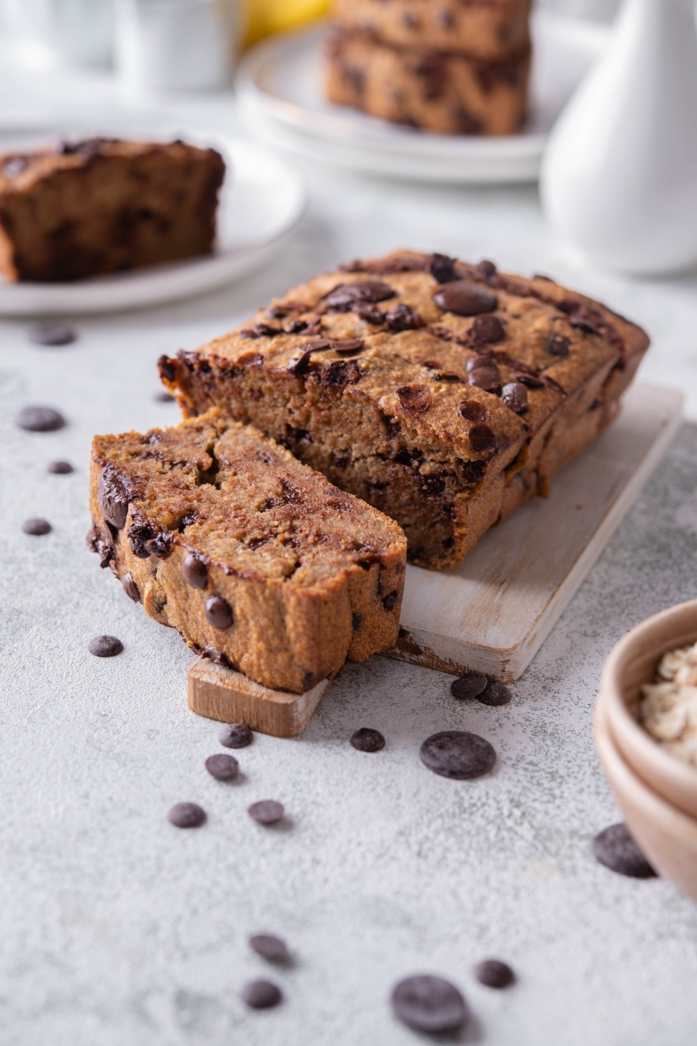 Sliced oatmeal chocolate chip banana bread on a wooden serving board, in front of two more plate of banana bread slices.