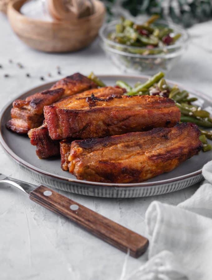 Roasted pork belly strips on a plate served with green bean salad. In the back is a small bowl of green bean salad.