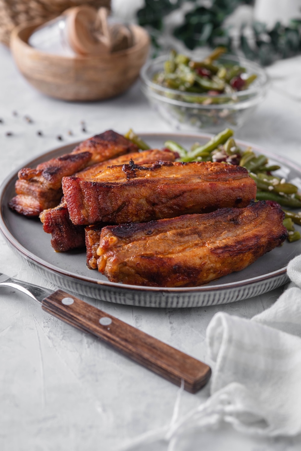 Roasted pork belly strips on a plate served with green bean salad. In the back is a small bowl of green bean salad.