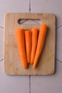 Four peeled carrots on a wooden cutting board.