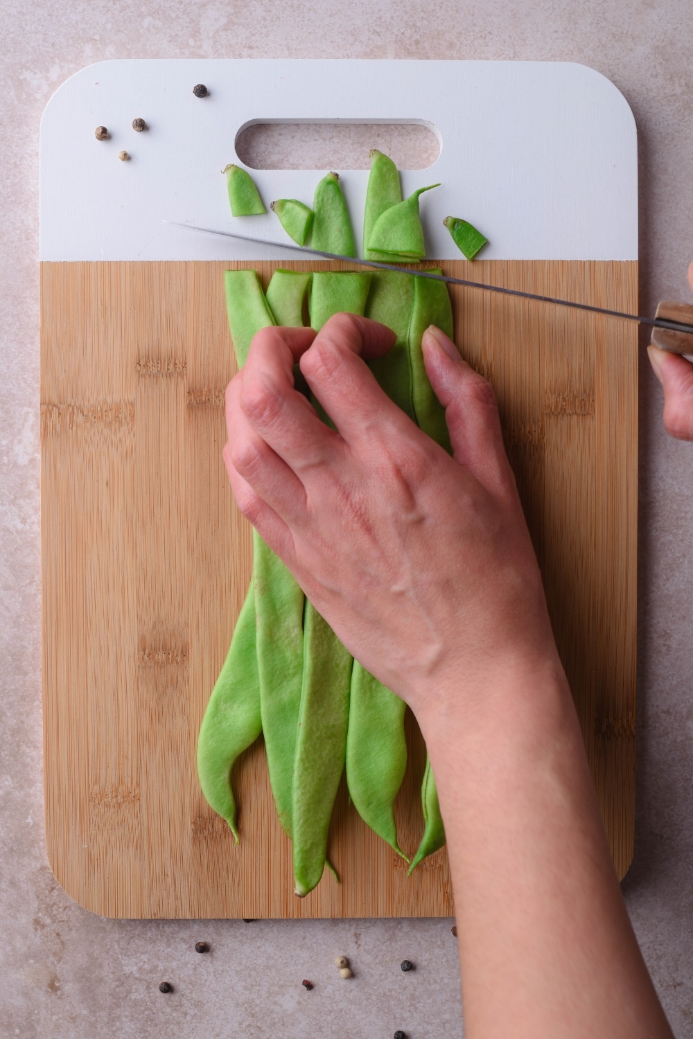 Trimming the ends off a bunch of green beans on a wooden cutting board.