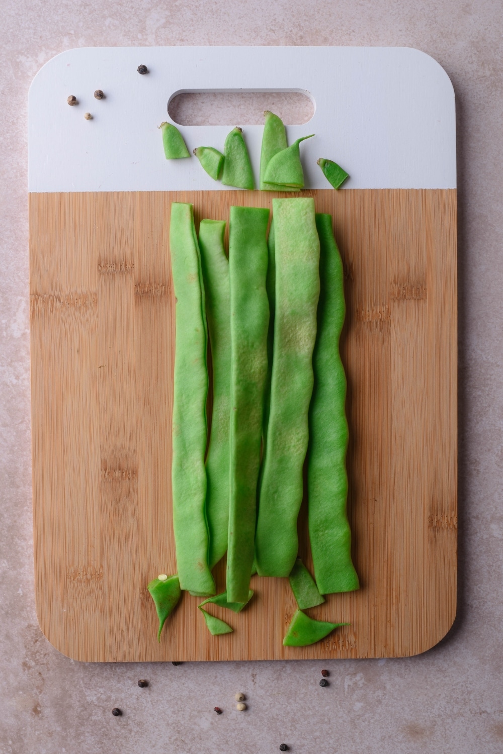 Trimmed green beans and their trimmed off ends on a wooden cutting board.