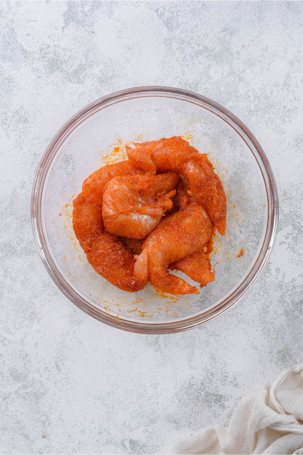 Season raw chicken tenders in a glass bowl.