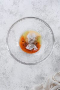 Glass bowl of olive oil, garlic powder, onion powder, paprika, salt, and pepper.