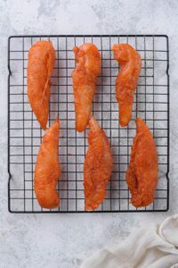 Six seasoned raw chicken tenders on a baking rack.
