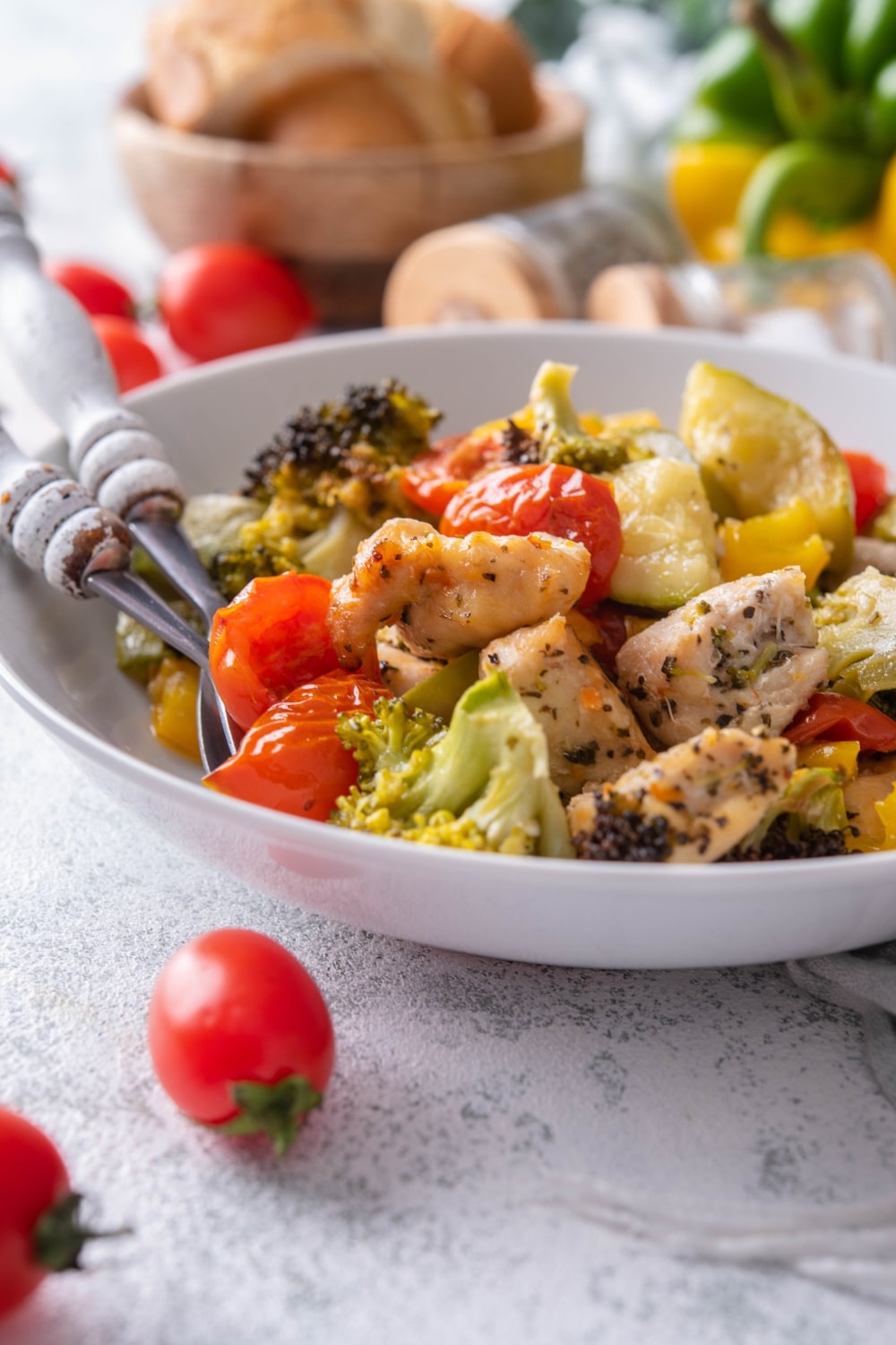 Close up of roasted chicken and veggies in a shallow white bowl.