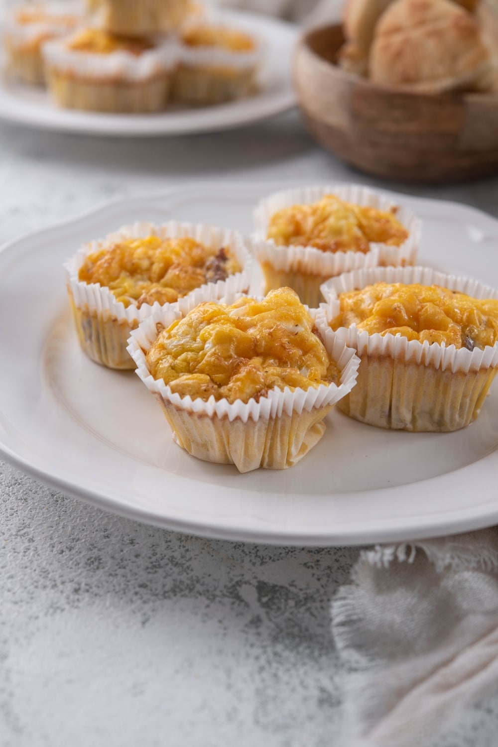 Four sausage egg muffins in muffin liners on a white plate.