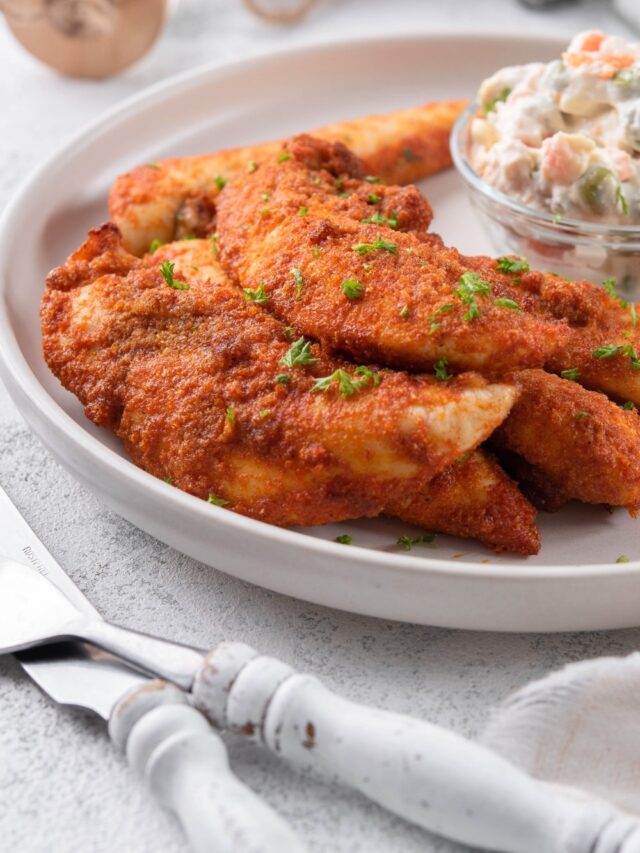 Baked chicken tenders garnished with chopped parsley with a small bowl of creamy potato salad.
