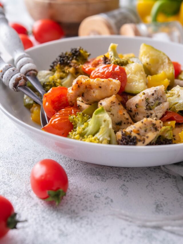 Close up of roasted chicken and veggies in a shallow white bowl.