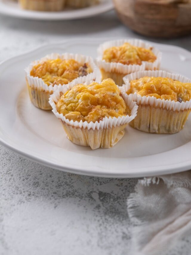 Four sausage egg muffins in muffin liners on a white plate.