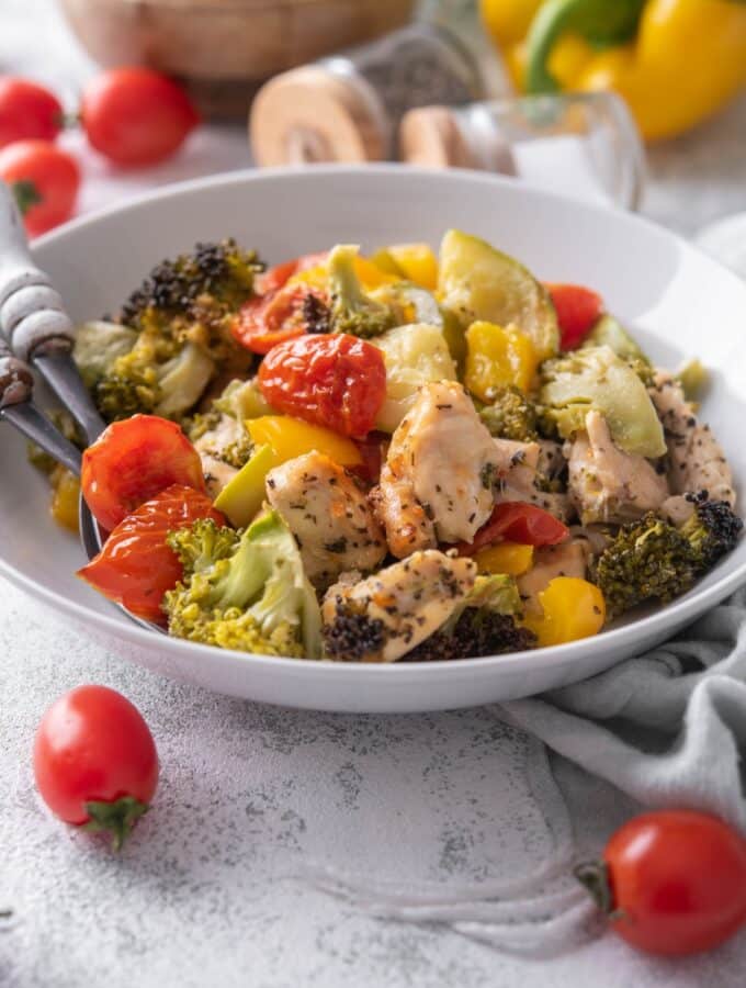 Roasted chicken and veggies in a shallow white bowl with two forks.