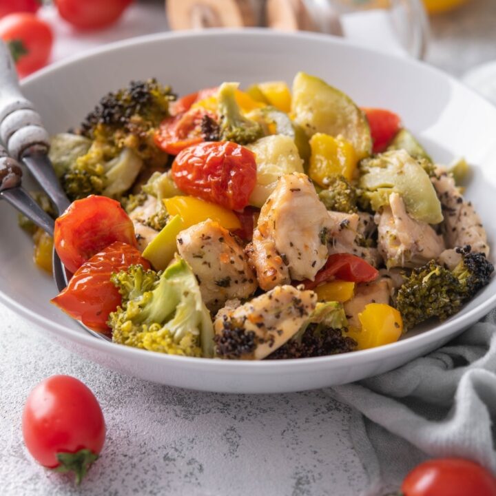 Roasted chicken and veggies in a shallow white bowl with two forks.